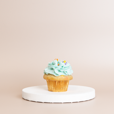 Vanilla cupcake in a gold foil liner topped with pale mint-blue buttercream and colorful confetti sprinkles