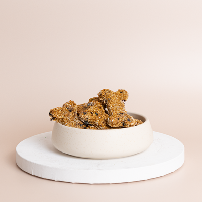 Rustic golden-brown handcrafted dog treats with visible berry and seed pieces piled in a cream ceramic bowl