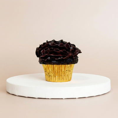 Dark chocolate cupcake in a gold foil liner topped with a thick ruffled swirl of glossy dark chocolate ganache