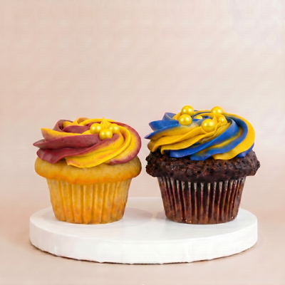 One vanilla cupcake with maroon and gold buttercream and one chocolate cupcake with blue and gold buttercream, each topped with gold pearl accents