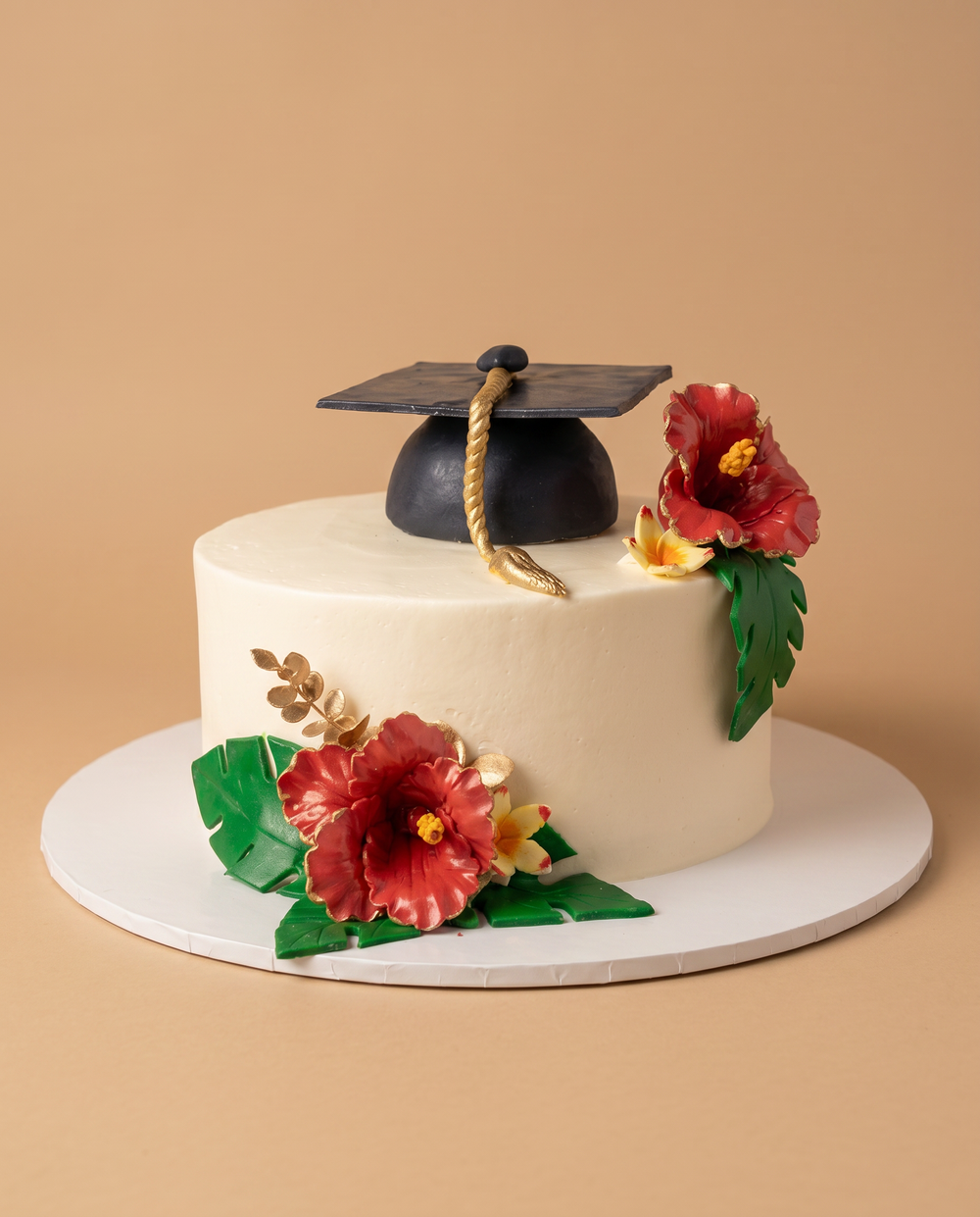 White buttercream graduation cake with a black fondant grad cap topper and red tropical hibiscus flowers