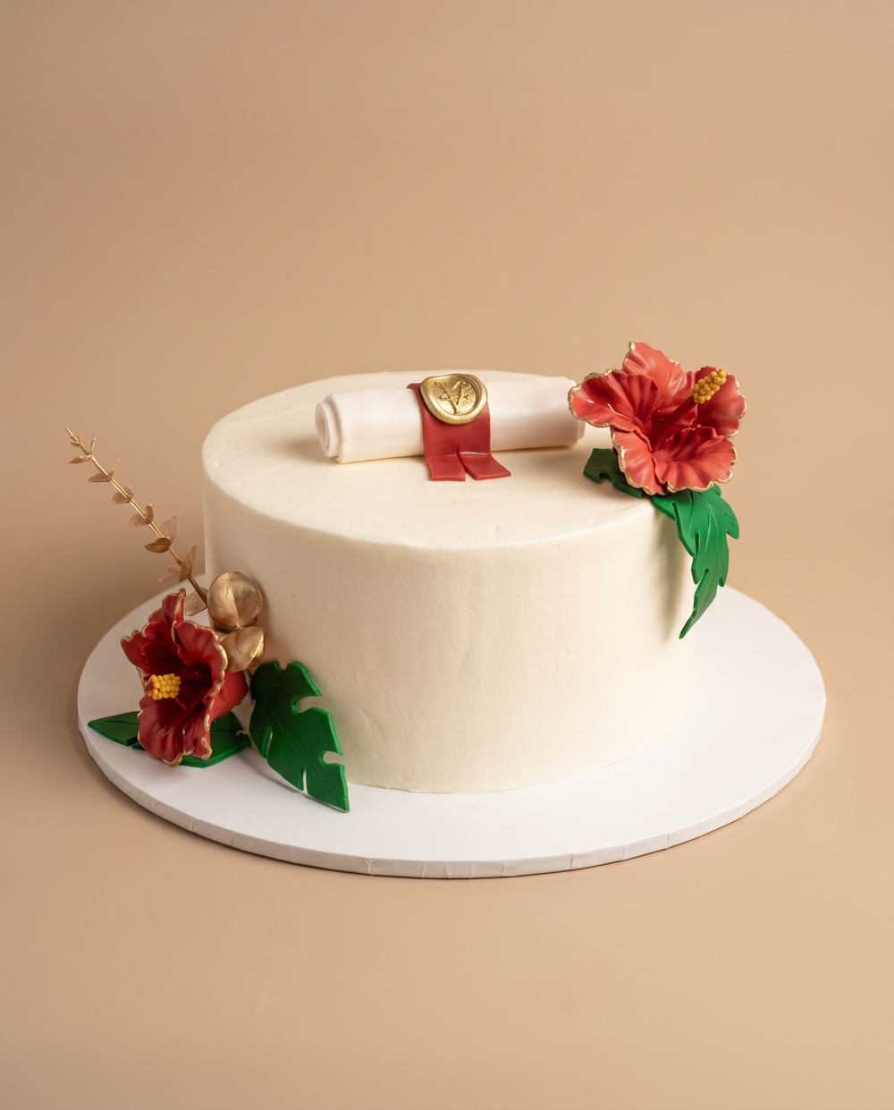 White buttercream graduation cake topped with a fondant diploma scroll and red tropical hibiscus flowers
