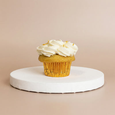 Vanilla cupcake in a gold foil liner topped with fluffy white whipped buttercream and delicate flecks of lemon zest