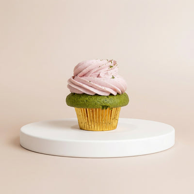  Cupcake in a gold foil liner with deep green matcha cake, topped with a pink strawberry buttercream swirl dusted with matcha powder