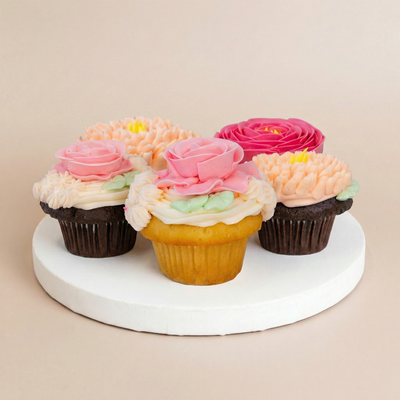Four chocolate and vanilla cupcakes each topped with a different buttercream flower — pink roses, a hot pink rose, and peach chrysanthemums with green leaves
