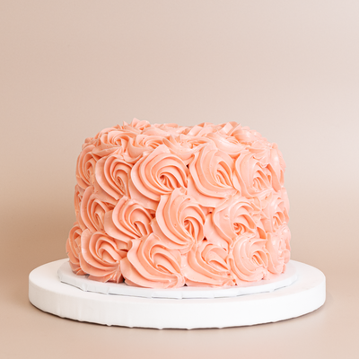 Tall single-tier round cake completely covered in densely piped peachy-pink buttercream rosettes, with swirled floral texture across every surface from base to top