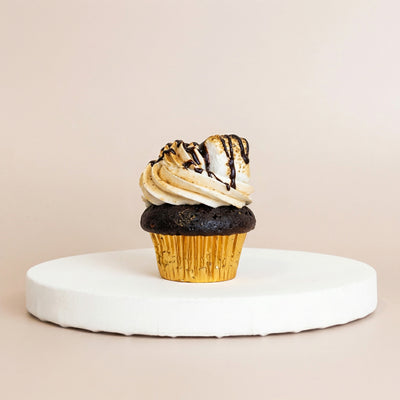 Chocolate cupcake in a gold foil liner topped with toasted vanilla buttercream, a torched marshmallow, and dark chocolate drizzle