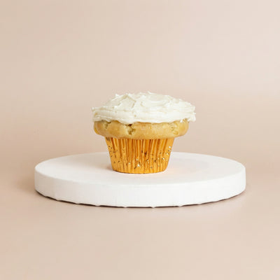 Vanilla cupcake in a gold foil liner topped with a smooth flat layer of white vanilla buttercream