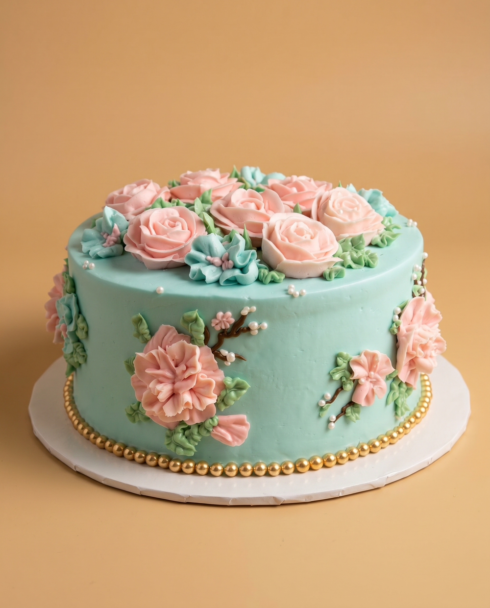 Teal buttercream cake with piped pink roses, carnations, and cherry blossoms with a gold pearl border
