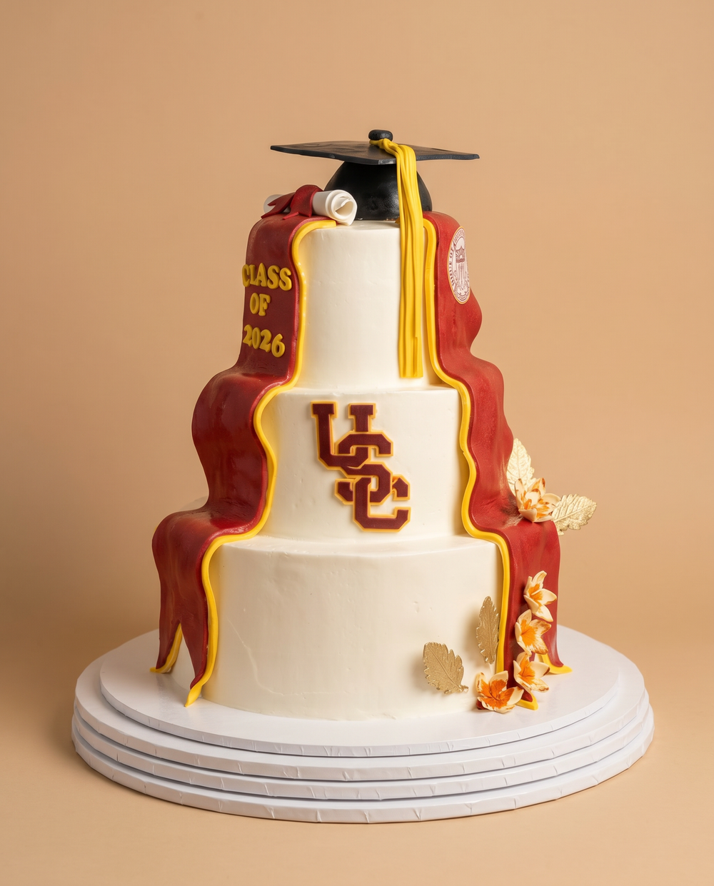 Three-tier USC graduation cake with cardinal and gold draping, Class of 2026 banner, and fondant grad cap topper