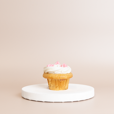 Vanilla cupcake in a gold foil liner topped with white buttercream and small pink buttercream flower accents
