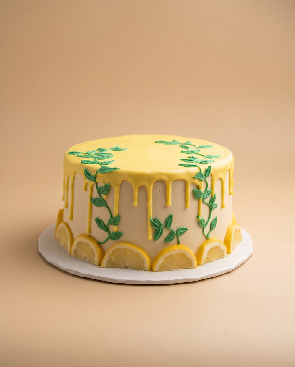 White buttercream lemon cake with yellow drip glaze, piped green vines, and fresh lemon slices around the base