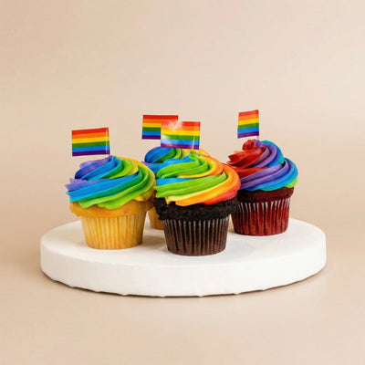 Four vanilla and chocolate cupcakes with swirled rainbow buttercream and mini Pride flag toppers