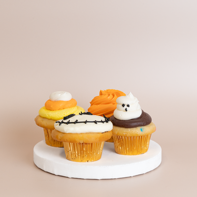 Four Halloween cupcakes in gold foil liners with candy corn, skeleton face, orange swirl, and white ghost buttercream decorations