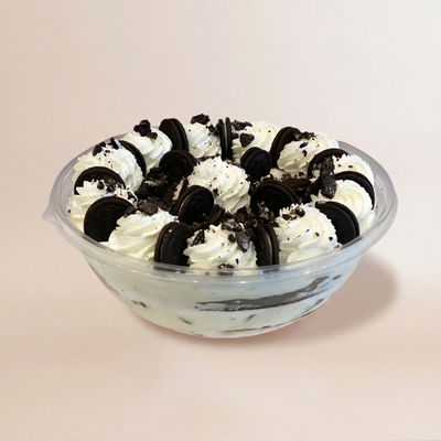 Large clear bowl of layered tiramisu with chocolate cake and cream visible through the sides, topped with whipped cream swirls and whole Oreo cookies