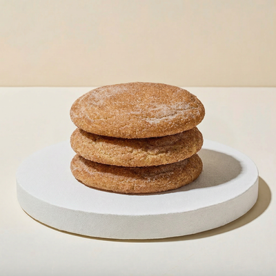 Three large flat round cookies stacked on a white pedestal, coated in cinnamon sugar with a warm sugary shimmer